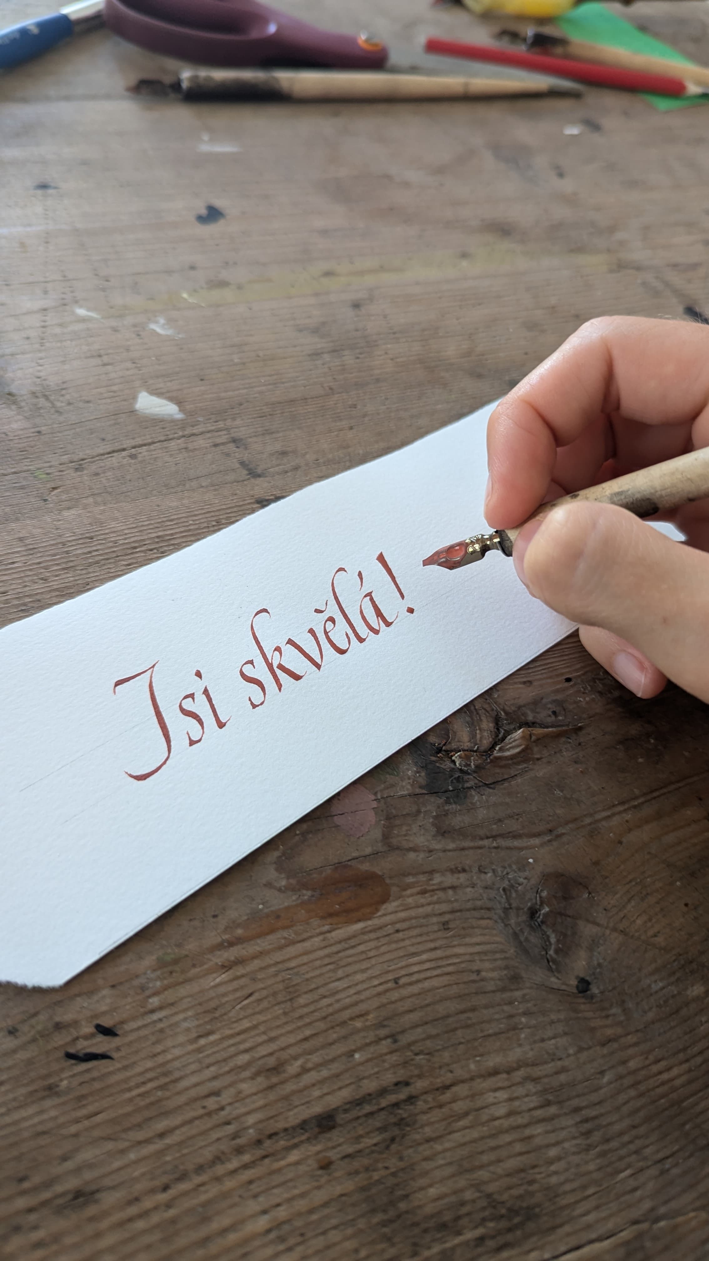 Ruka kaligrafky píše italikou nápis ‚Jsi skvělá!' špičatým perem.